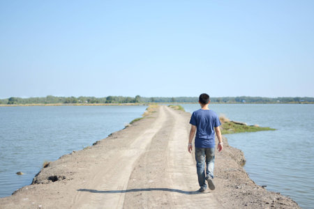 Young man walking along walkway near the lakeの写真素材