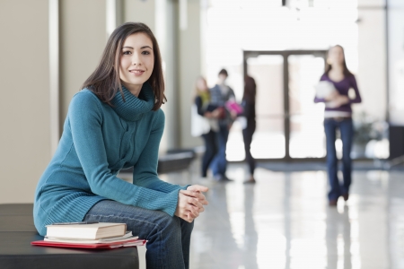 Asain American student sitting on bench with books in hall between classesの写真素材
