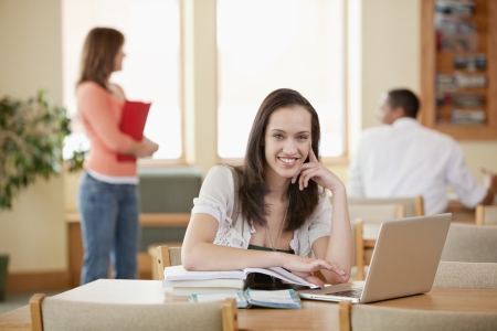 Female student seated at table with books   laptop in libraryの写真素材