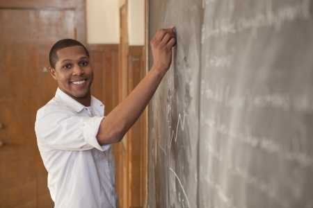 African American student happily writting on a chalkboard in classromの写真素材