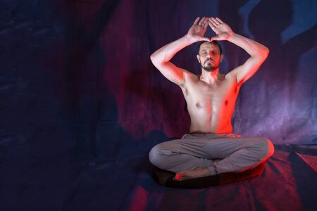 A man sits in a lotus position. Male European 40-45 years old. A man is engaged in meditation. The man raised his arms above his head. Magic and occultism.の写真素材