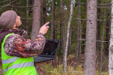 Ecologist watches the growth of trees in the forest. Forest officer with a computer works in the forest. Forestry and afforestation.の写真素材