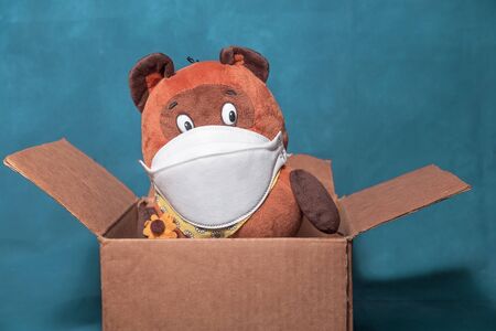 Cardboard box with a toy. Toy with a medical mask. The concept of the spread of viral diseases.
