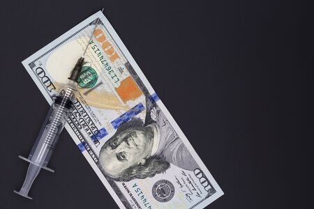 Medical syringe on a black background. On the syringe hangs a bill of 100 dollars. The concept of...