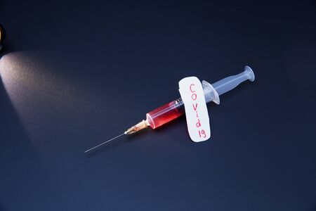 Medical syringe with a vaccine. Label with the inscription "COVID-19". Dark background.の写真素材