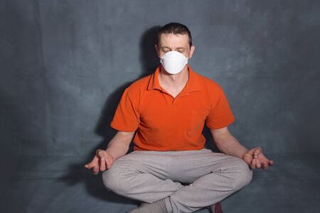 A man in a medical mask sits in a lotus position. The concept of calm attitude to the pandemic covid-19.の写真素材