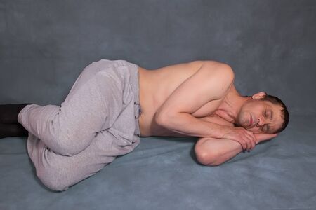 A 40-year-old European man lies and sleeps. Gray background.