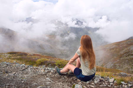 Young woman looks at mountains and clouds. Travel and tourism concept.の写真素材