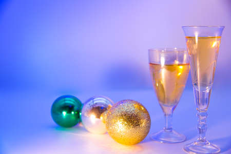 Christmas background. Spruce green branches. New Year's toys hang on fir branches. Glasses with a drink. Beautiful colored lighting.の写真素材
