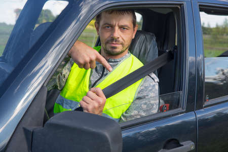 A 40-year-old European man in the cab of a car, wearing a seat belt. Points to the belt. Safe...