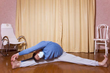 A European man, 40 years old, practices yoga in a medical mask. A person is engaged in gymnastics at...