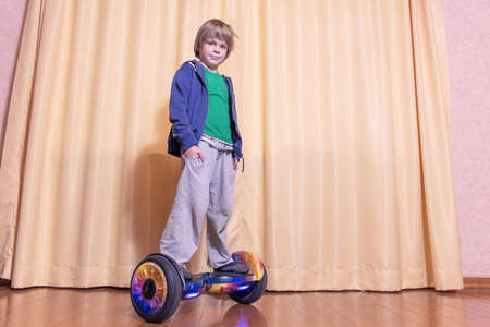 A five-year-old European boy is learning to ride a hoverboard in a room at home.