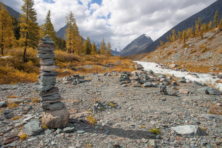 A pyramid of stones is built on the banks of a mountain river. Selective focus on the pyramid. In the background there are high mountains with a glacier.の写真素材