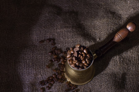 The coffee maker is on a rough sacking. Whole coffee beans have been poured into the coffee maker. Dark background, selective focus on coffee beans.の写真素材