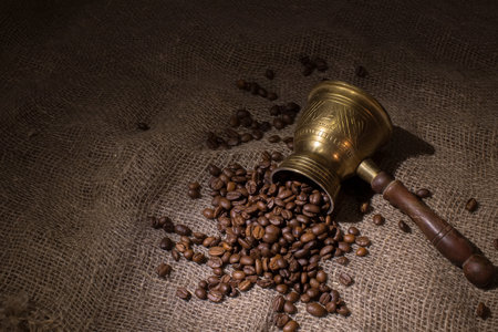 The coffee maker lies on a rough sacking. Coffee beans are scattered on the fabric. Dark background, selective focus on the coffee beans.の写真素材