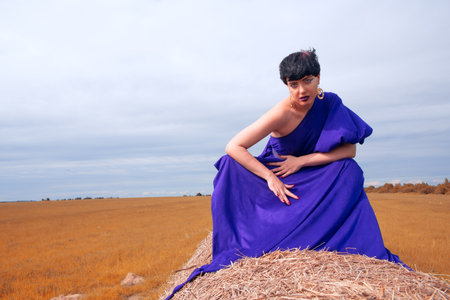 Woman in a blue dress against the background of the field and the sky.