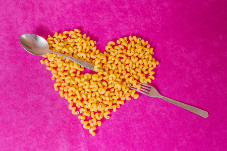 Macaroni lie on a pink background. A spoon and a fork lie next to the pasta. The concept of eating pasta.の写真素材