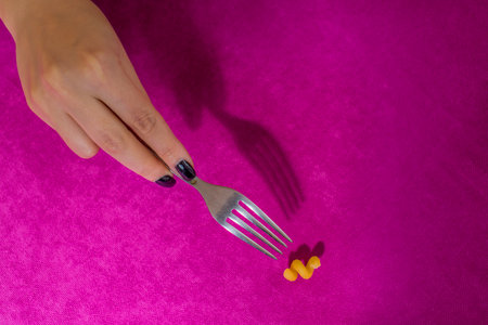A female hand holds a fork. The fork clings to the pasta. Pink background.の写真素材
