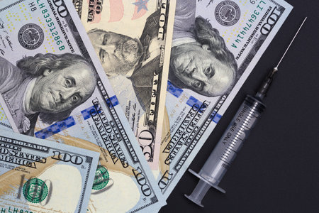 Dollar bills and a medical syringe lie on a dark background.の写真素材
