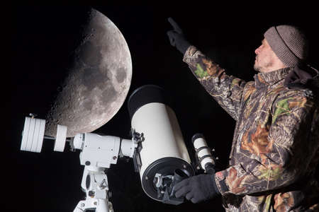 A European man observes the moon through a telescope. The man points his finger at the moon.
