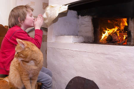 The boy sits near the Russian stove with the cat.の写真素材