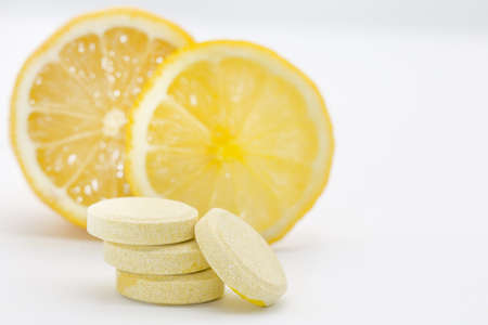 Vitamin "C" tablets on a white background. Cut lemons in the background.の写真素材