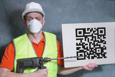 Worker in a medical mask. A builder with a working tool holds a dummy QR code in his hand.の写真素材
