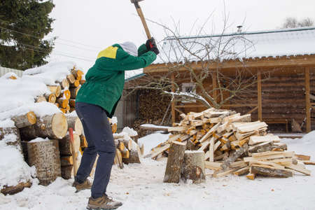 A man chops wood with a large ax. Photo of a man in motion. Soft focus. Small snowflakes all over the image field.の写真素材