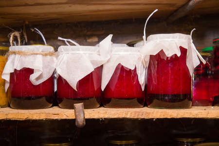 Glass jars of berry jam stand on a wooden shelf in the basement. soft focus.の写真素材