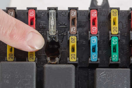 The finger points to burnt contacts in the fuse box. On the body of the block, the designs of electrical circuits are applied.の写真素材