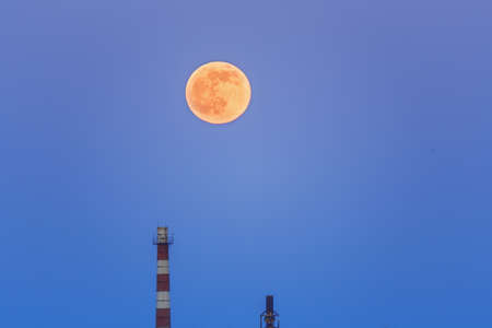 A large moon in the evening sky above the industrial pipes of the plant.の写真素材