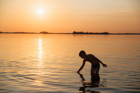 Silhouette of a child playing in the water against the backdrop of a beautiful sea sunset.の写真素材