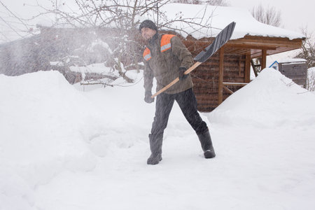 A man in work clothes removes snow in the yard of his house. Snow dust flies in the air.の写真素材