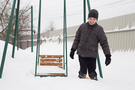 a boy stands knee-deep in the snow near a children's swing.の写真素材