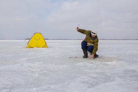 A man is engaged in winter fishing on a frozen lake.の写真素材