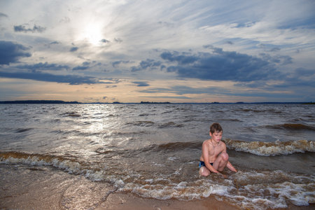 A boy plays in the water on the shore of a lake.の写真素材