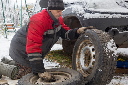 A European man changes wheels with summer tires on a car to wheels with winter tires.の写真素材