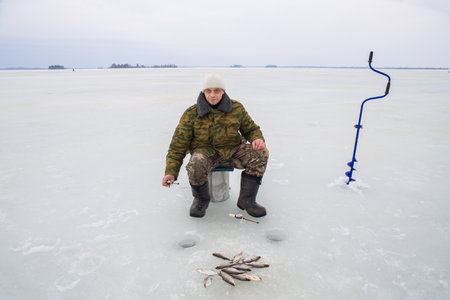 A European man fishes on the ice of a frozen lake. Looks at the camera.の写真素材