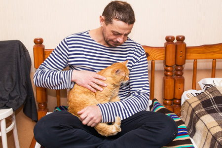 A European man, 49 years old, is stroking a beautiful ginger cat.の写真素材