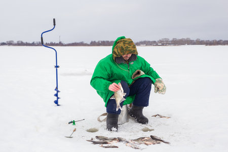 A 49-year-old European man fishes on the ice of a lake. holding a caught fish in his hands, looking to the side.の写真素材