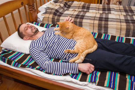 A man, 49 years old, is stroking a beautiful ginger cat.の写真素材
