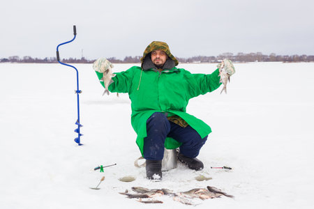A 49-year-old European man fishes on the ice of a lake. holding a caught fish in his hands, looking at the camera.の写真素材