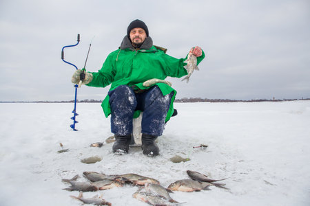 A 49 year old European man is fishing on the ice of a frozen lake. He is looking at the camera. He is holding a fish in his hands.eの写真素材