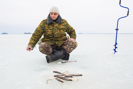 A man, European, 49 years old, is fishing on the ice of a lake.の写真素材
