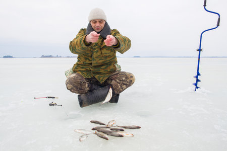 A man, European, 49 years old, is fishing on the ice of a lake.の写真素材