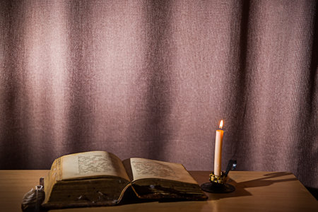 An old book lies open on the table. A candle burns in a candlestick nearby.の写真素材