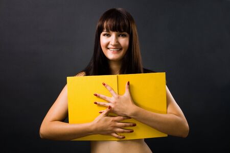 Sexy young woman with yellow book on blackの写真素材