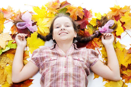 Happy teenager girl lay in maple leafs on white backgroundの写真素材