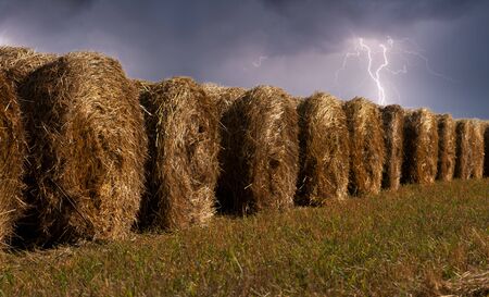 haystacks in the field during the thunderstorm with lightning in the sky