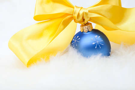 Christmas ball with yellow ribbon bow on white fur backgroundの写真素材